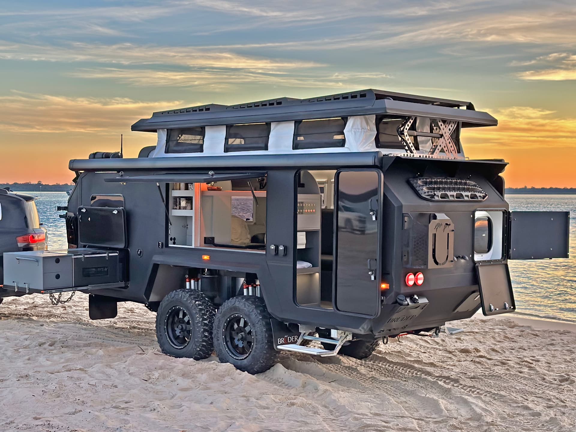 Bruder EXP camper opened up on a sand flat at sunset with hatches and drawers deployed