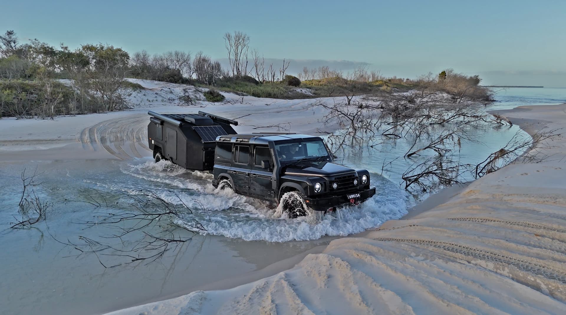 Black 4WD towing a Bruder EXP-4 through shallow beach water at dusk
